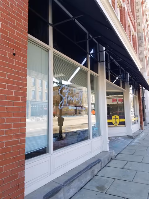 Exterior brick storefront with large windows and Stowell signage reflected in glass.