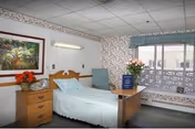 Bright resident room featuring a single bed, floral wallpaper, and a table with flowers.