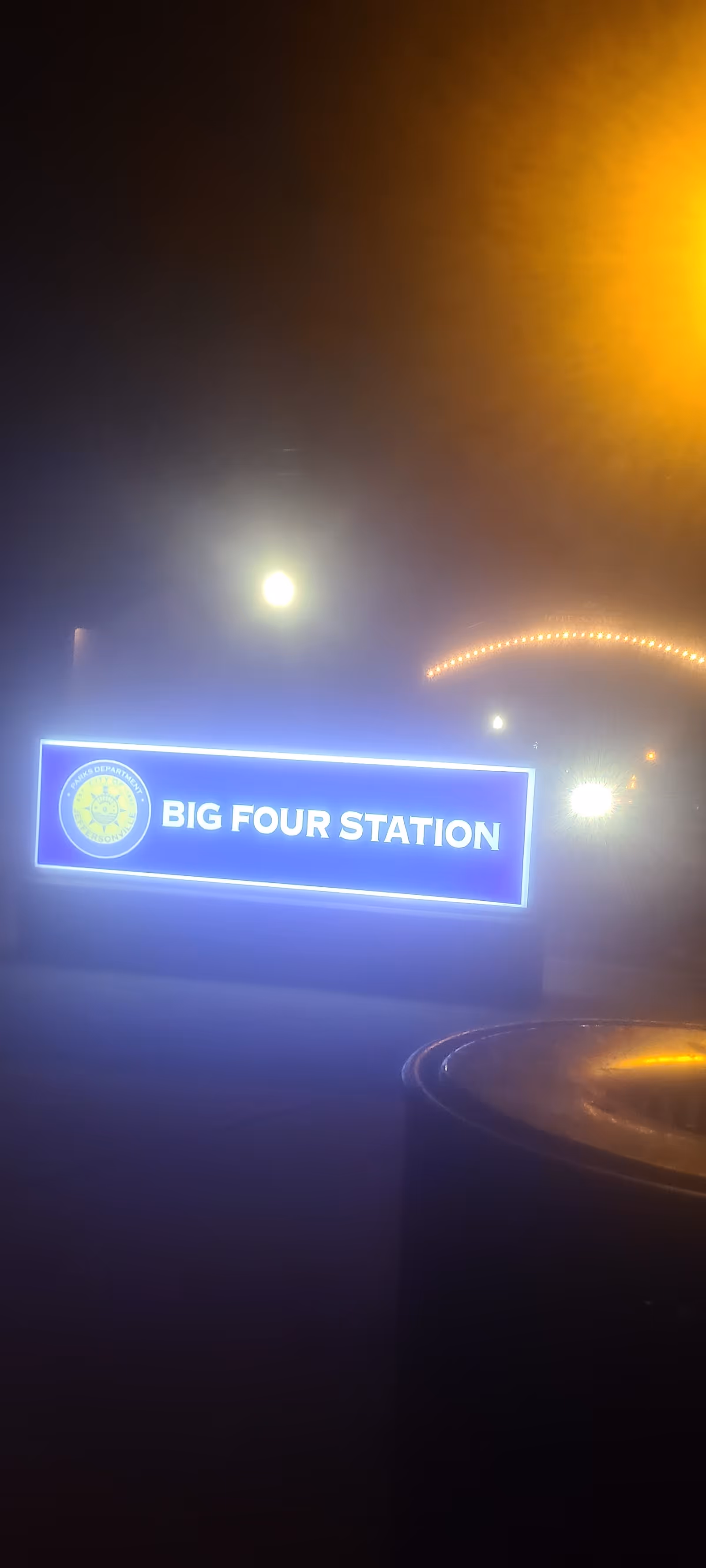 Nighttime exterior view of a glowing blue 'BIG FOUR STATION' sign at a facility entrance