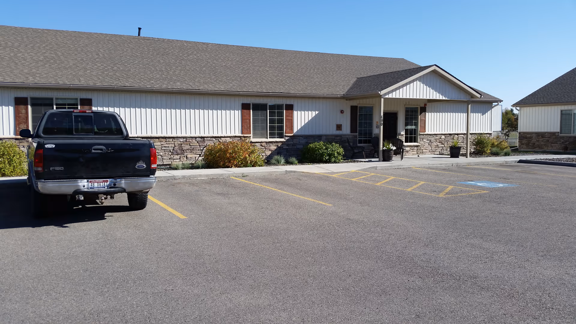 Front exterior of a single-story assisted living building with a parking lot and a black pickup truck parked near the entrance.