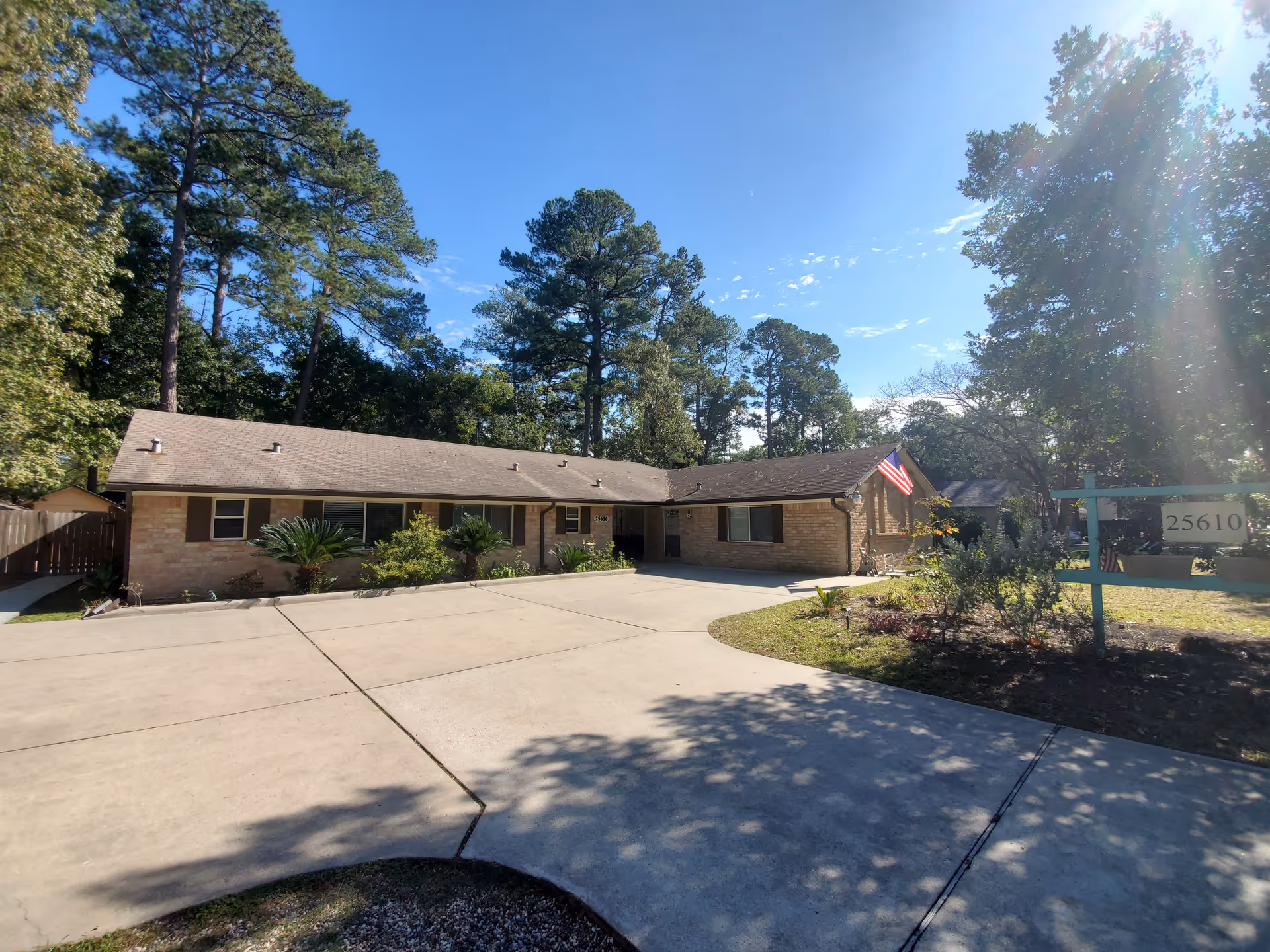 Single-story brick senior care facility with driveway, trees, and an American flag