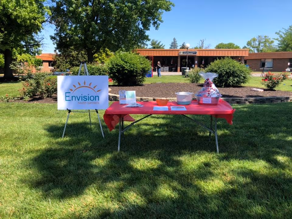 Outdoor grassy area with a red table, Envision Health Partners sign, and building in background.