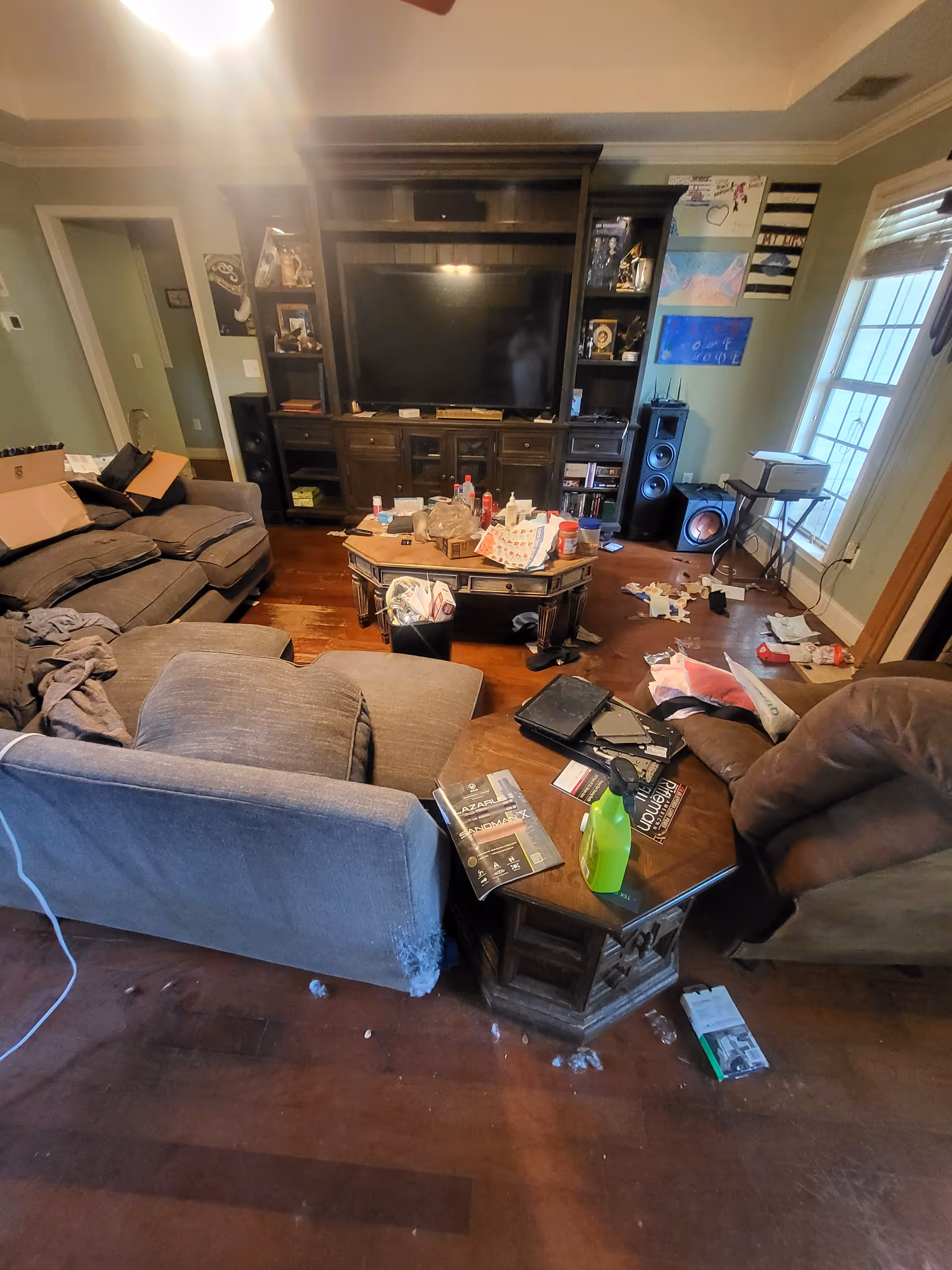 Messy living room with sofa, coffee table, TV unit, and scattered papers.