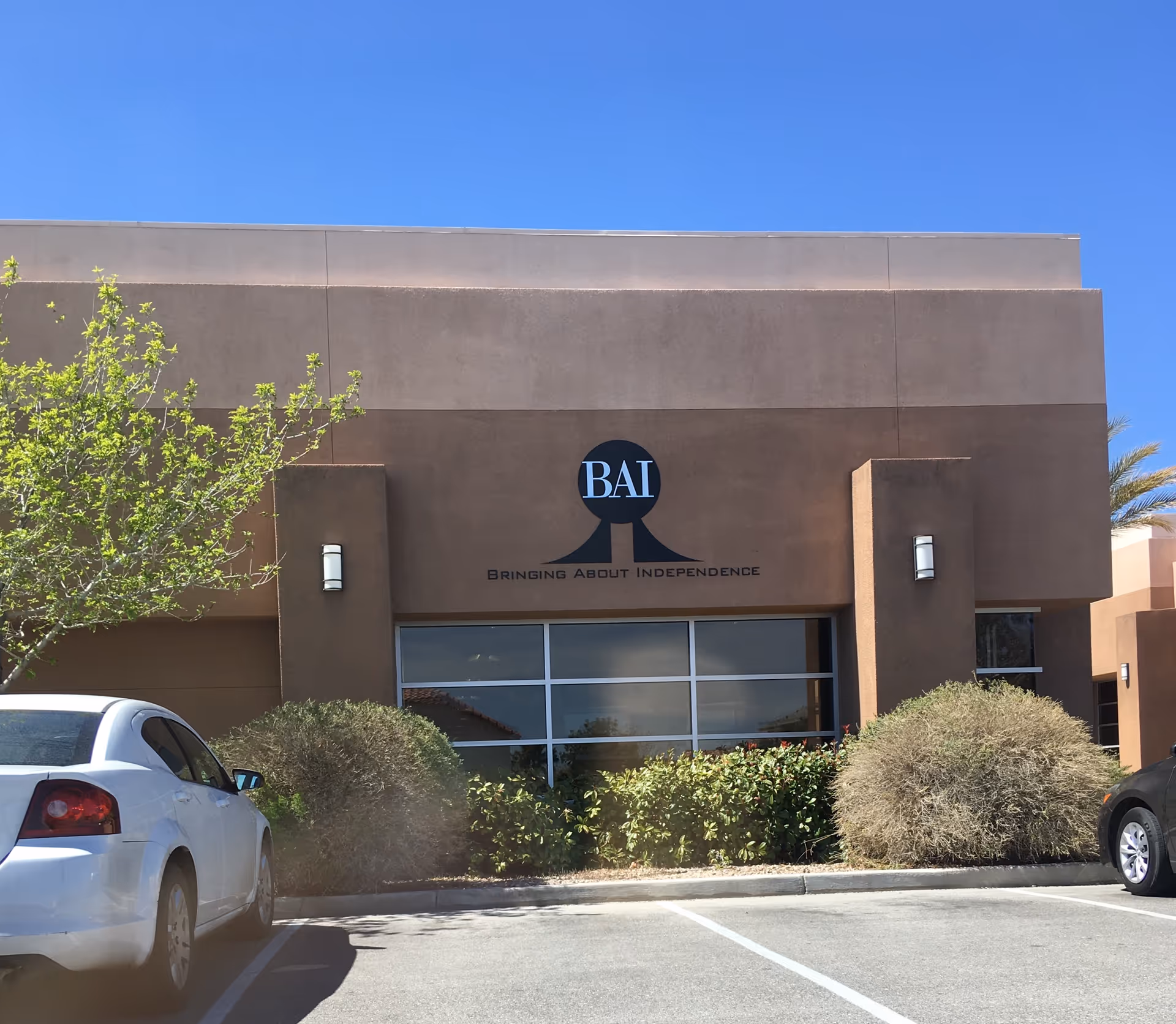Brown exterior of a senior living facility with BAI logo and parked cars.