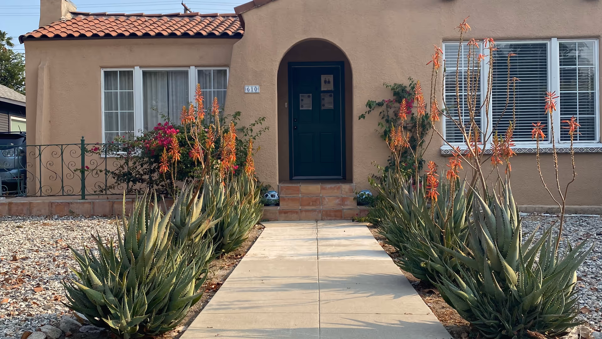 Desert landscaping lines a walkway to a teal front door of a beige stucco building.