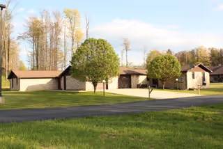 Exterior view of a single-story nursing home complex with stone walls, green lawn, and trees.