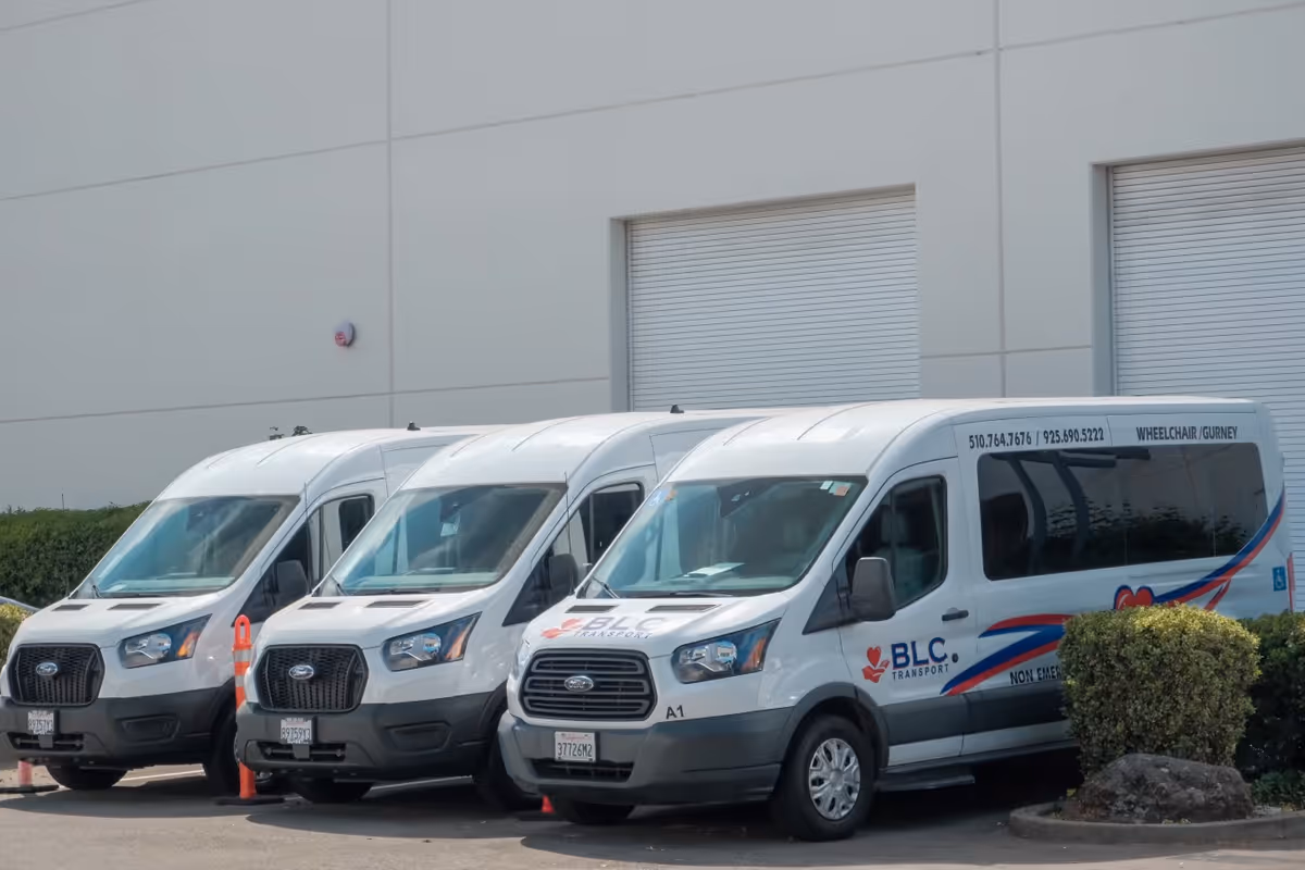 Three white shuttle vans parked outside Best Living Care facility.