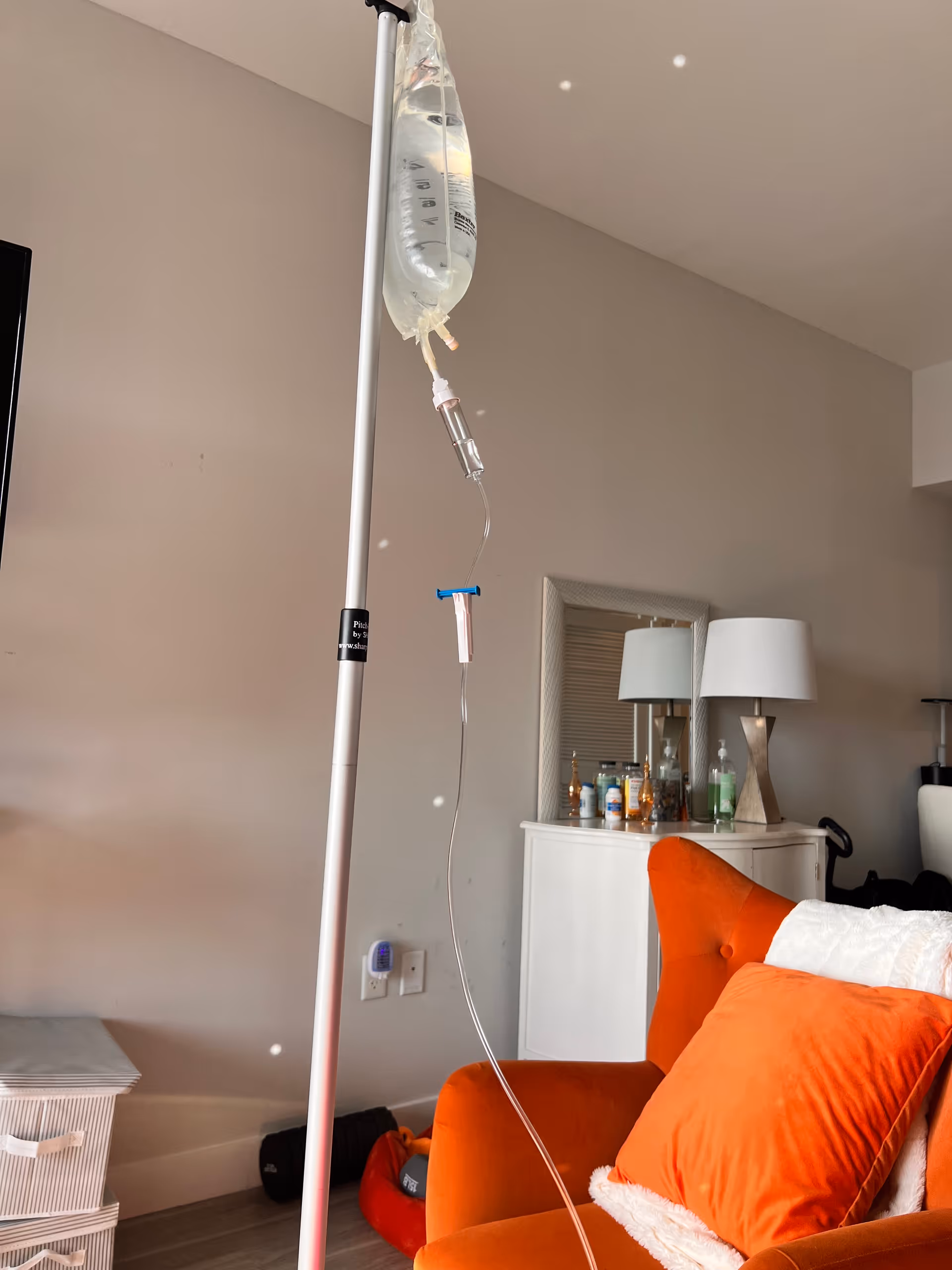 IV drip bag on pole in a living room with orange chair and dresser