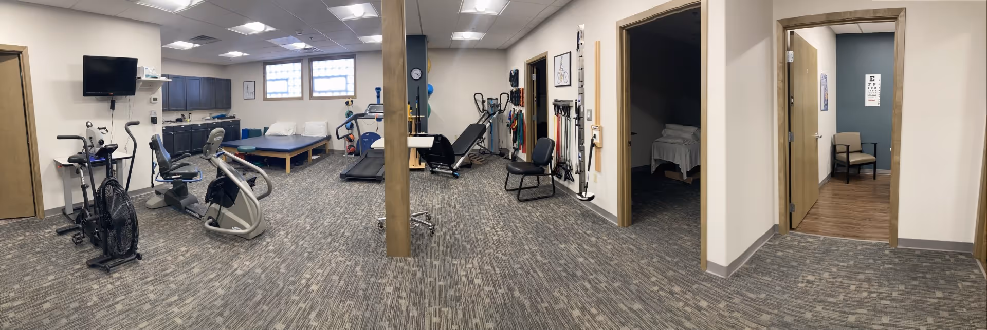 Wide interior view of a senior facility gym with exercise equipment and adjacent rooms.