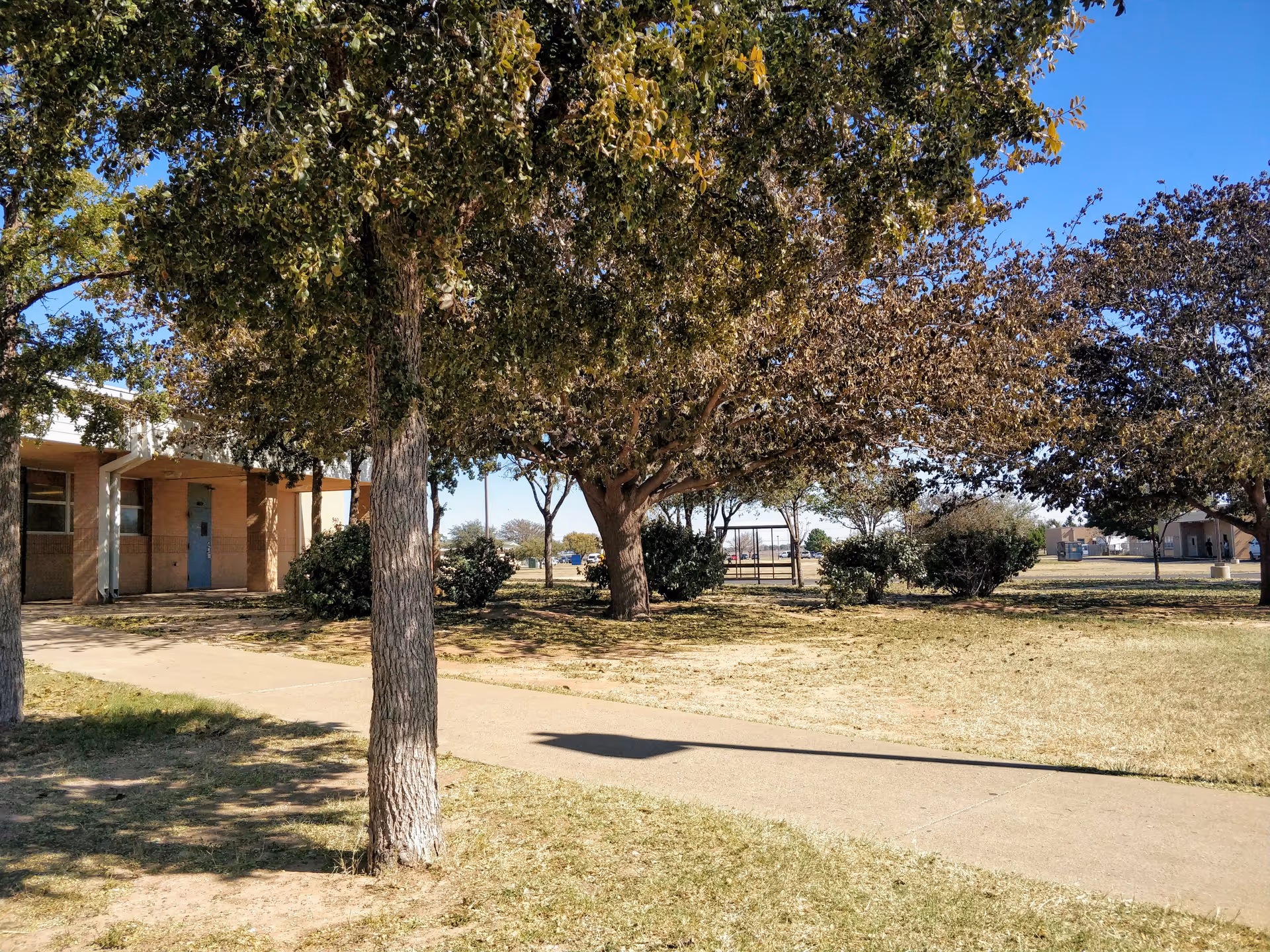 Sunny outdoor scene with a walking path, trees, and a small brick building at the facility.