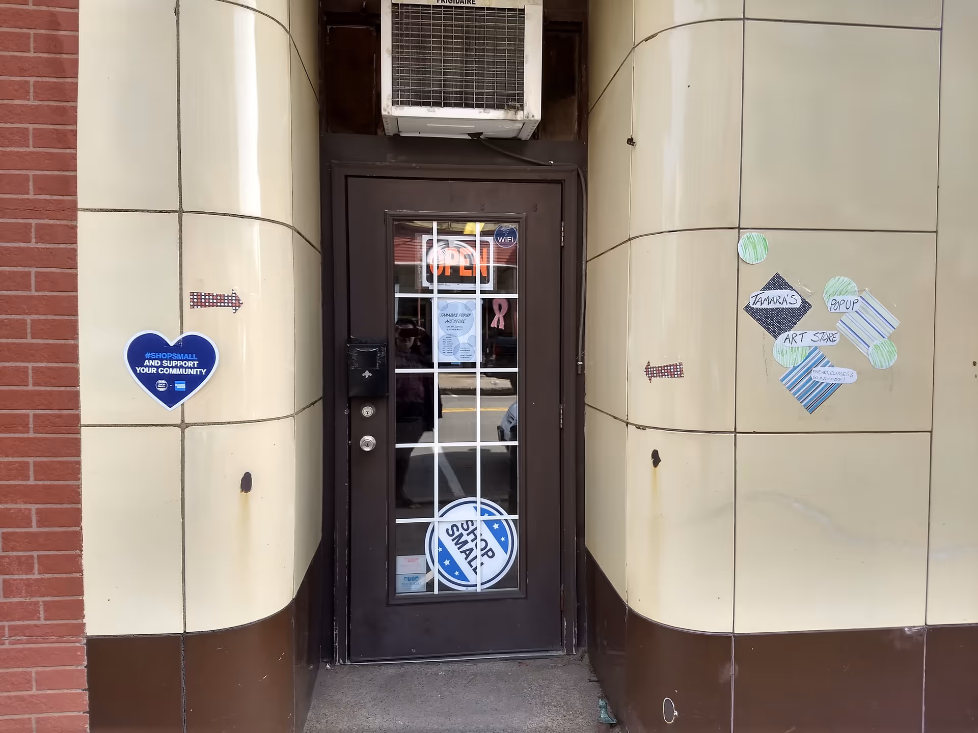 Exterior building entrance with glass door between beige columns, open sign, and stickers.