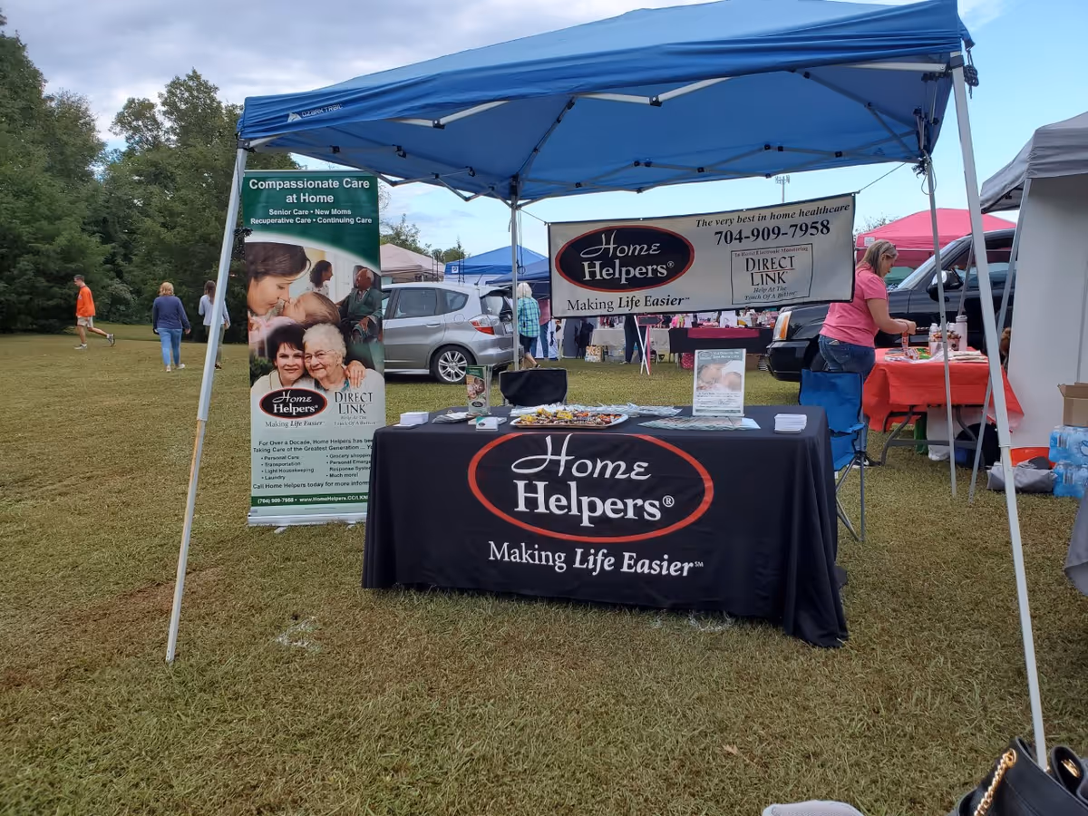 Blue canopy tent over a Home Helpers booth with banners and a table on grass.