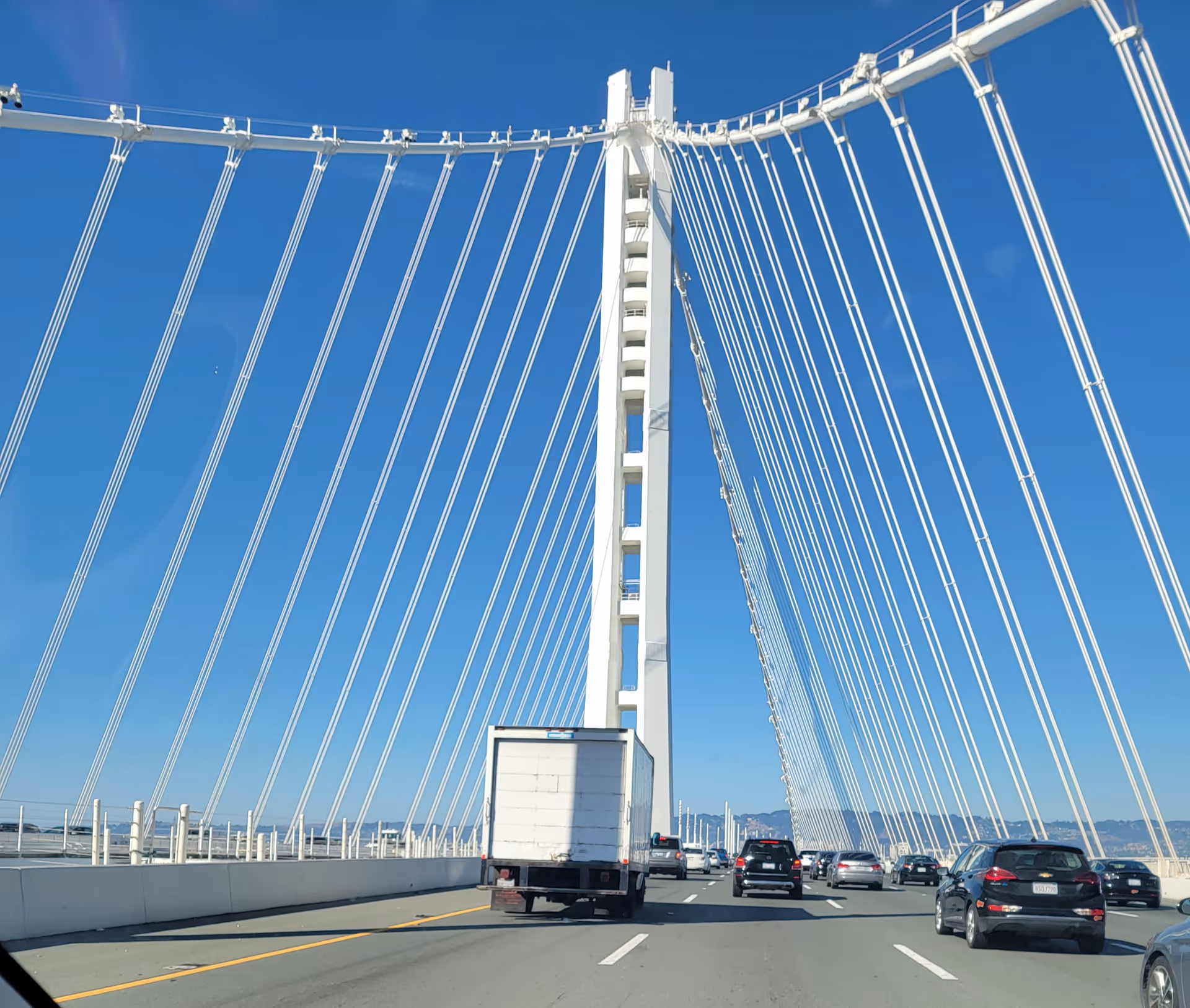 A modern suspension bridge with white towers and numerous cables against a blue sky.