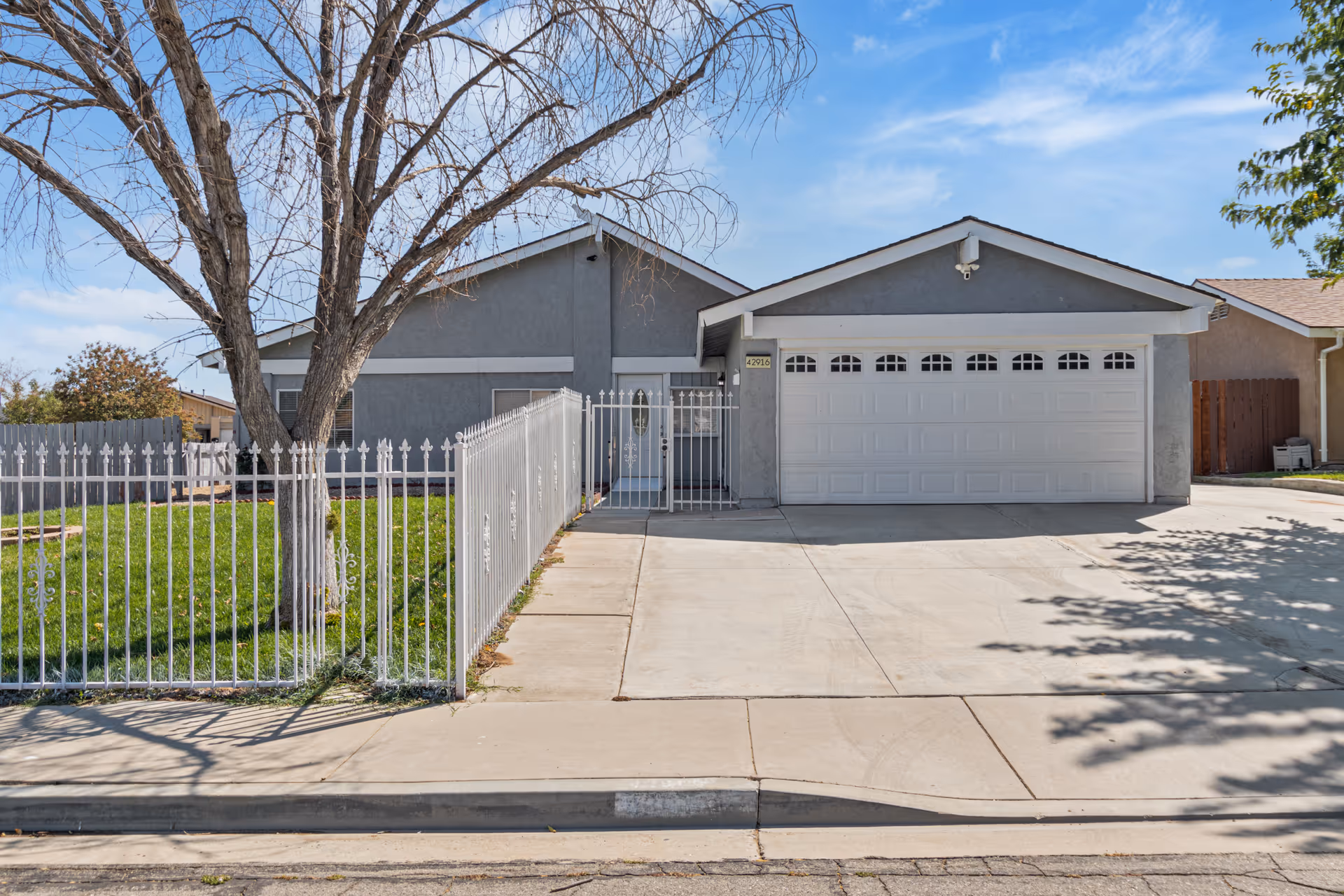 Single-story house with a two-car garage, white fence, and green lawn.