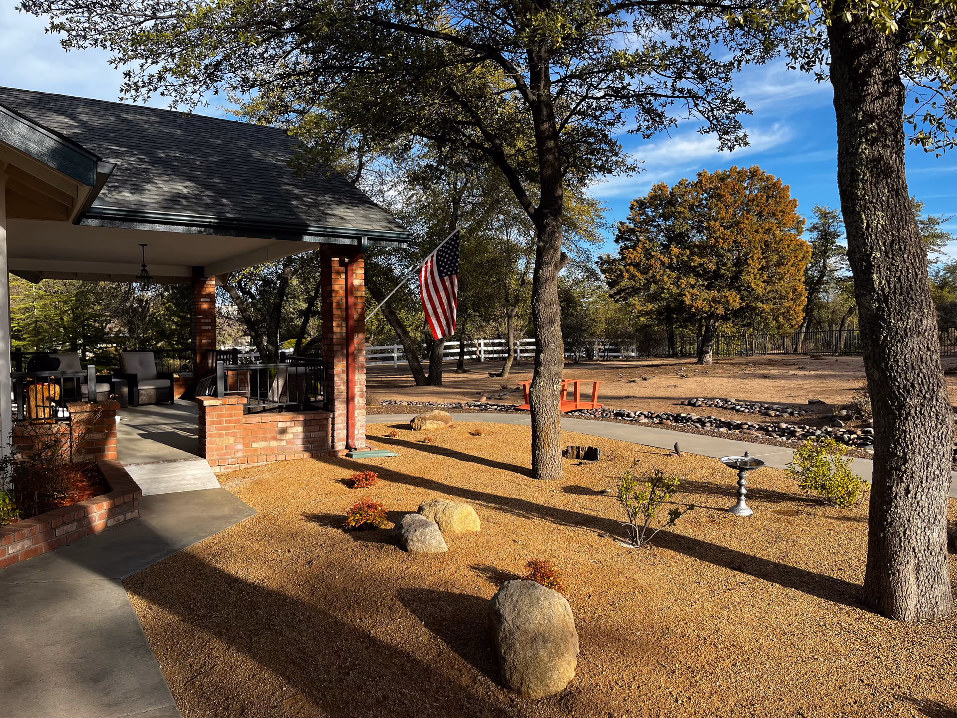 Exterior view of Summit Senior Living entry: brick porch, American flag, and tree-filled yard.