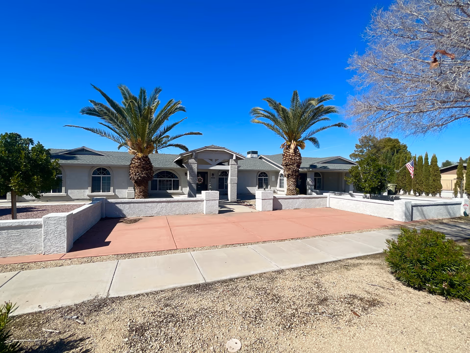 Front view of a single-story care home with two palm trees under a bright blue sky.