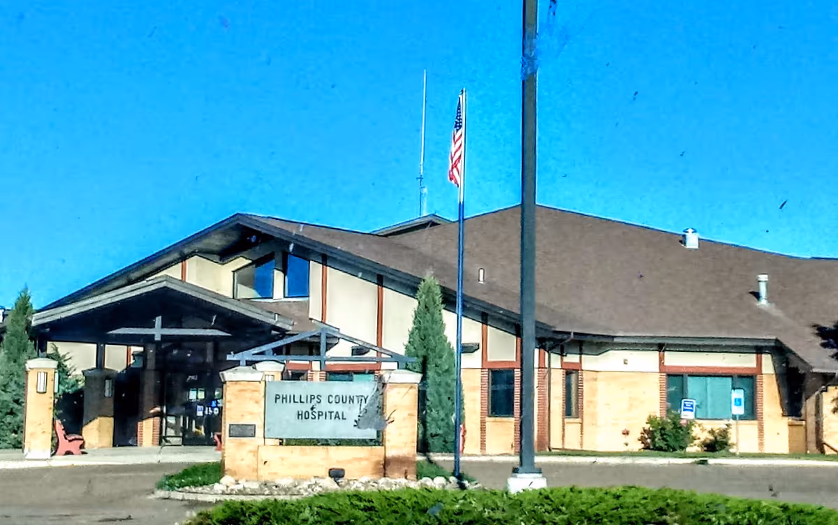 Exterior view of Phillips County Hospital entrance with flag, sign, and driveway.