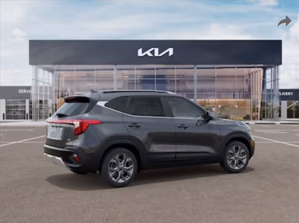 Gray SUV parked in front of a modern Kia dealership with large glass windows.