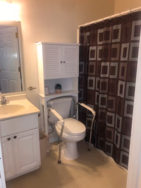 Bright bathroom with white vanity, toilet, grab bars, and geometric shower curtain.
