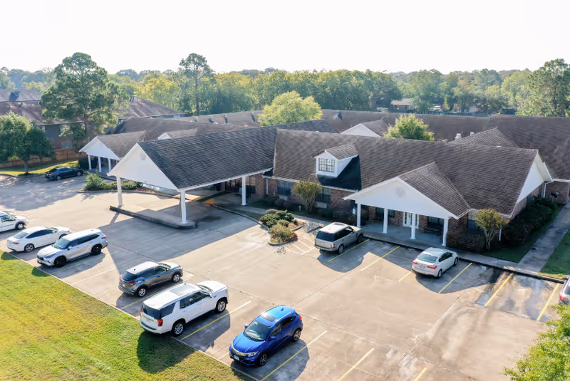 Aerial view of Cambridge Square Assisted Living exterior with parked cars and connected, gabled buildings.