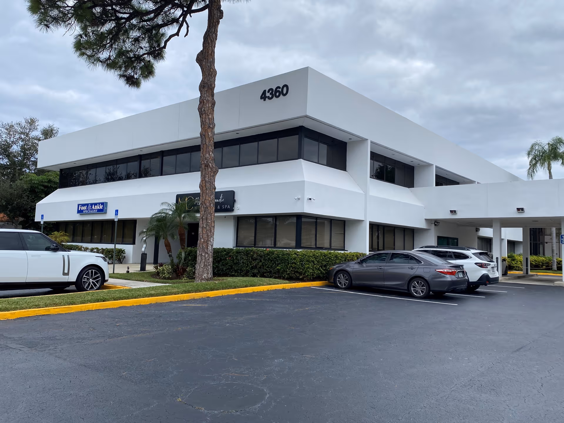 Modern white building with address 4360, a parking lot, and nearby palm trees.