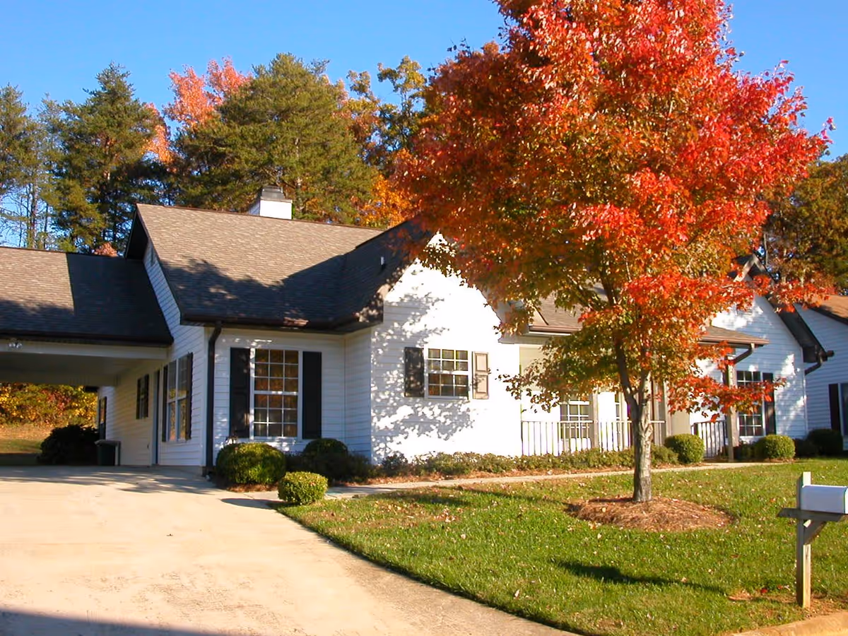 White single-story building with a driveway, a red-leaved autumn tree and a mailbox on a sunny day.
