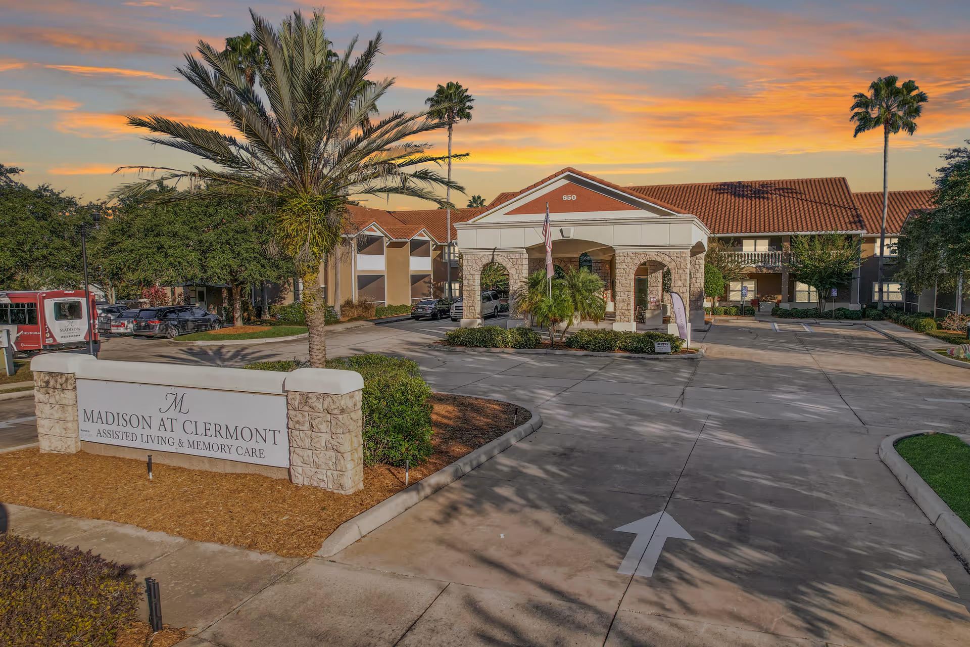 Exterior view of Madison at Clermont facility with sign and entrance surrounded by palm trees