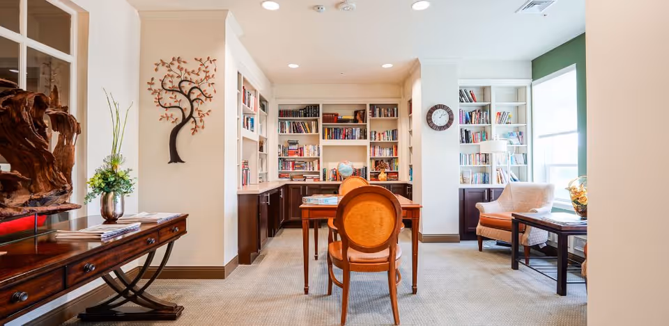 Cozy interior library and reading room with built-in bookshelves, a wooden desk, and comfortable seating.
