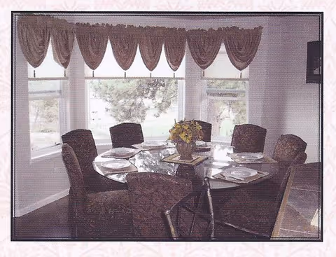 A round glass dining table with six chairs and a floral centerpiece indoors.