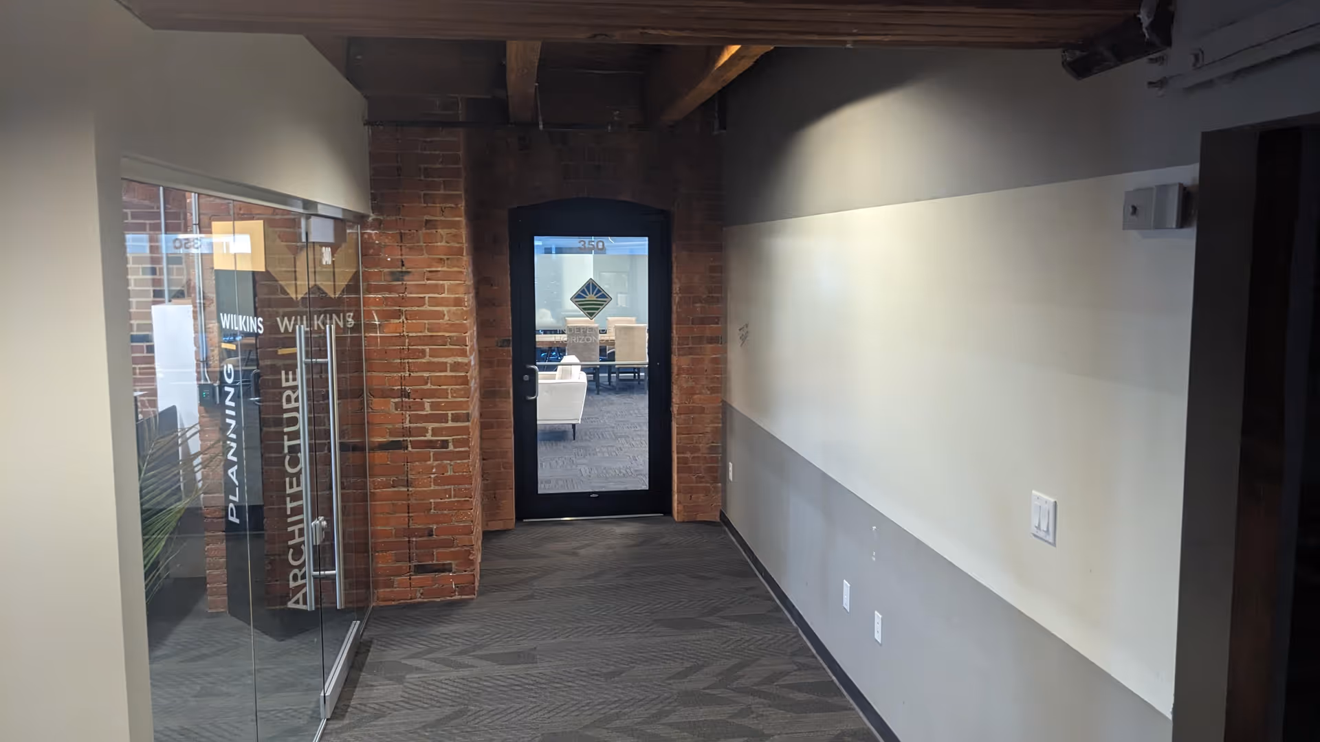 Interior hallway featuring brick columns, glass offices, and a doorway leading to a meeting room.