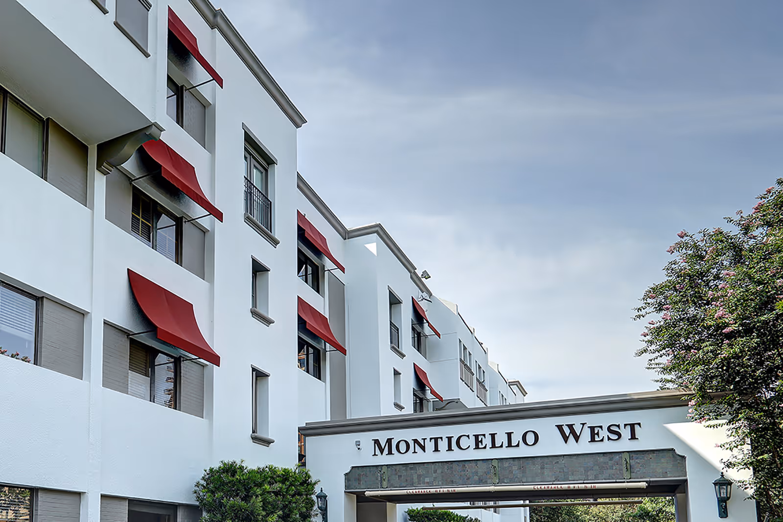 White, multi-story Monticello West building with red awnings and an entrance sign.