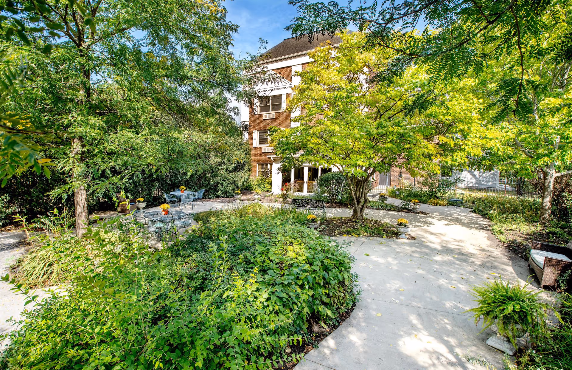 Landscaped courtyard with trees, patio tables, and a brick building entrance visible in the background.