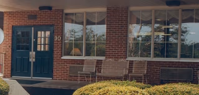 Front entrance of a brick senior living facility with benches and large windows.