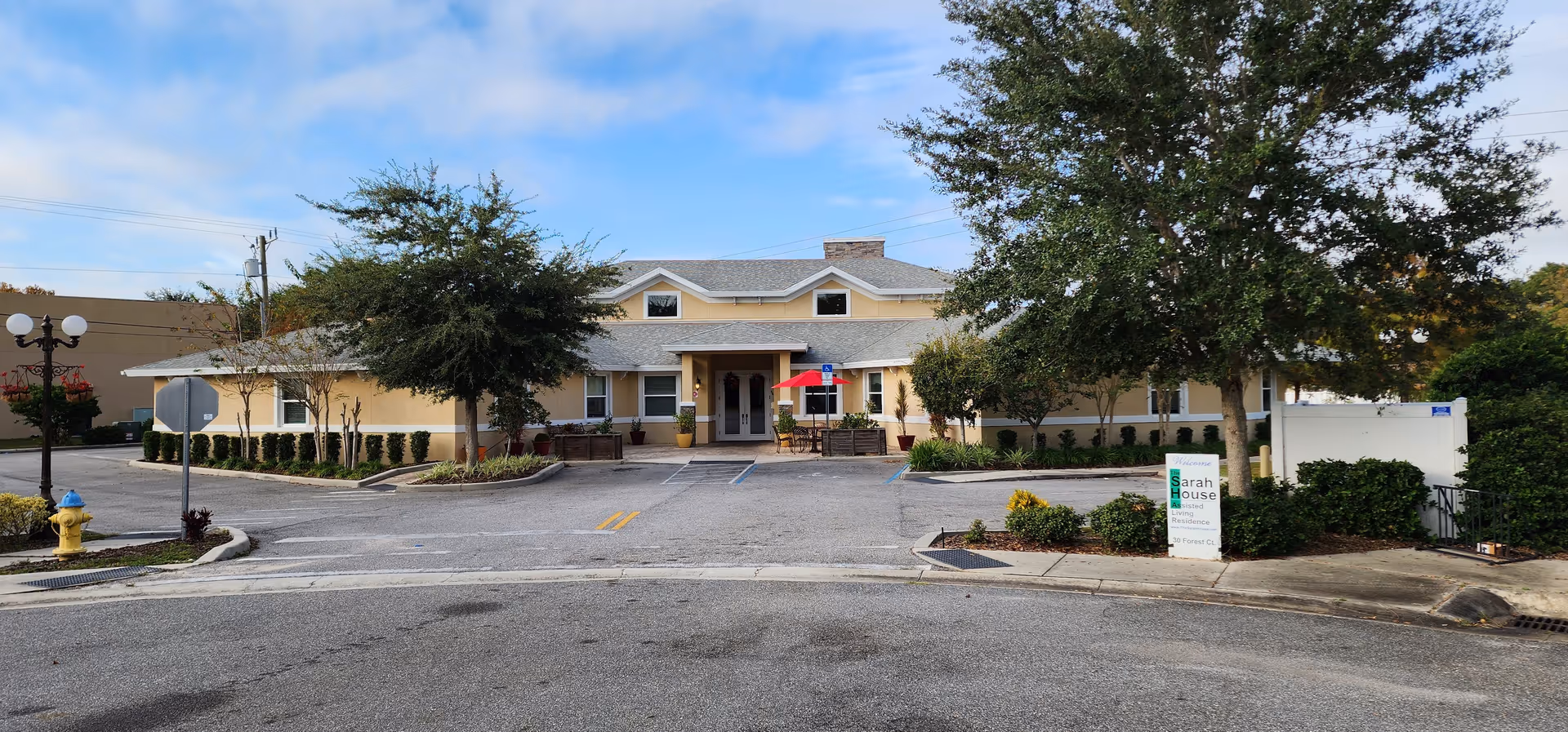 Single-story beige senior living facility with entrance, parking lot, and landscaped front yard.