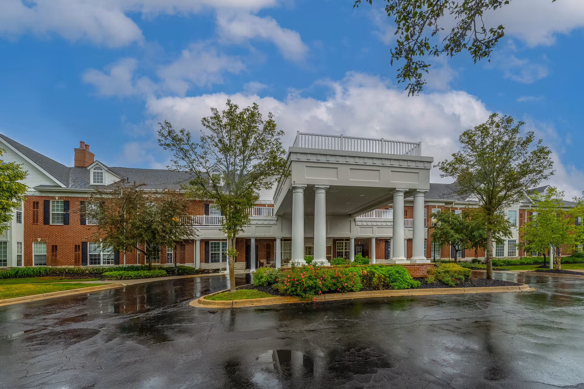 Waltonwood Twelve Oaks exterior with a columned porte-cochère, brick facade, and landscaped grounds.