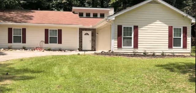 Front view of a single-story light-colored cottage with red shutters, a central door, and a green lawn.