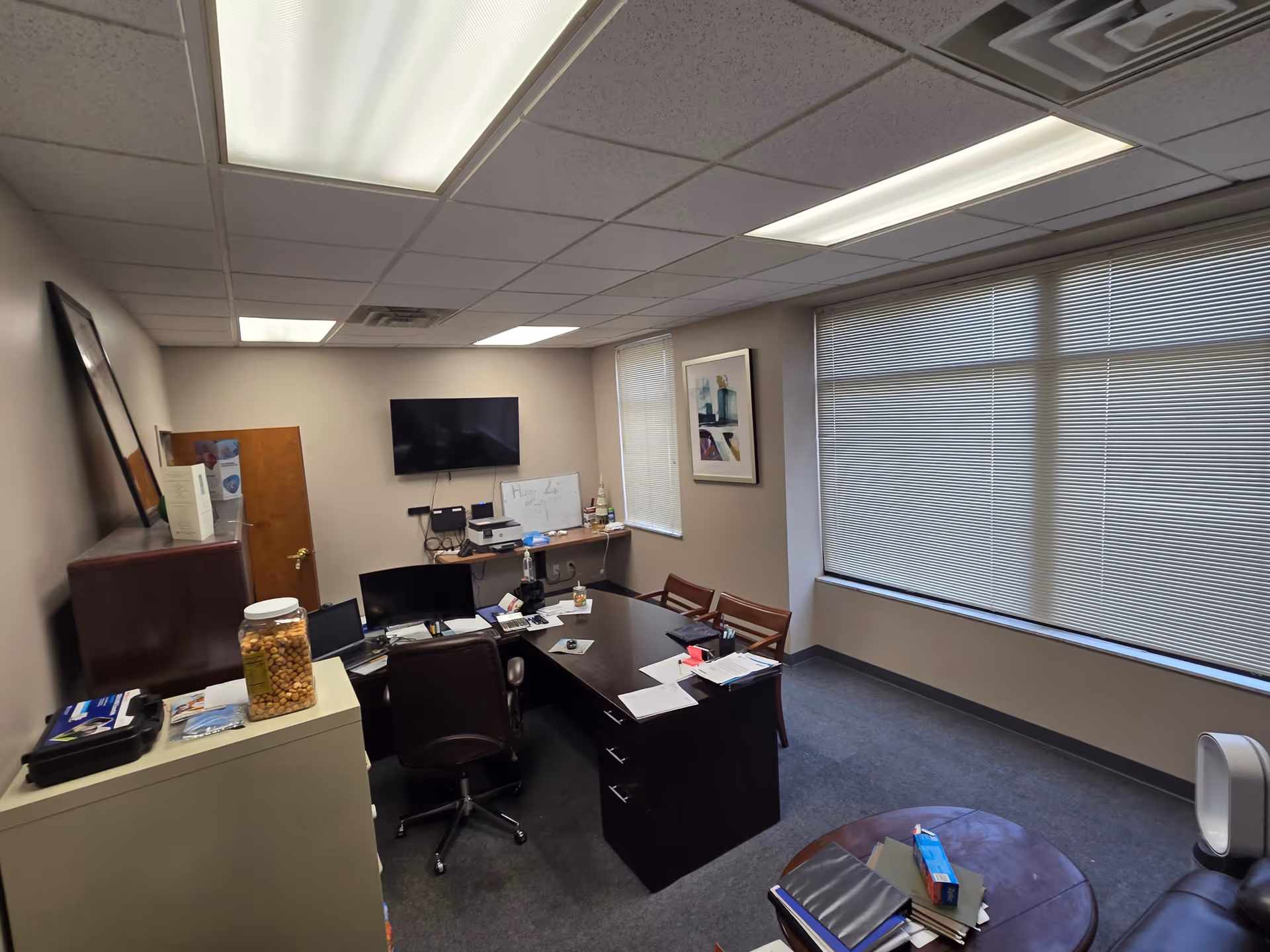Office inside Good Hands Home Care with desk, computer, whiteboard, and blinds.