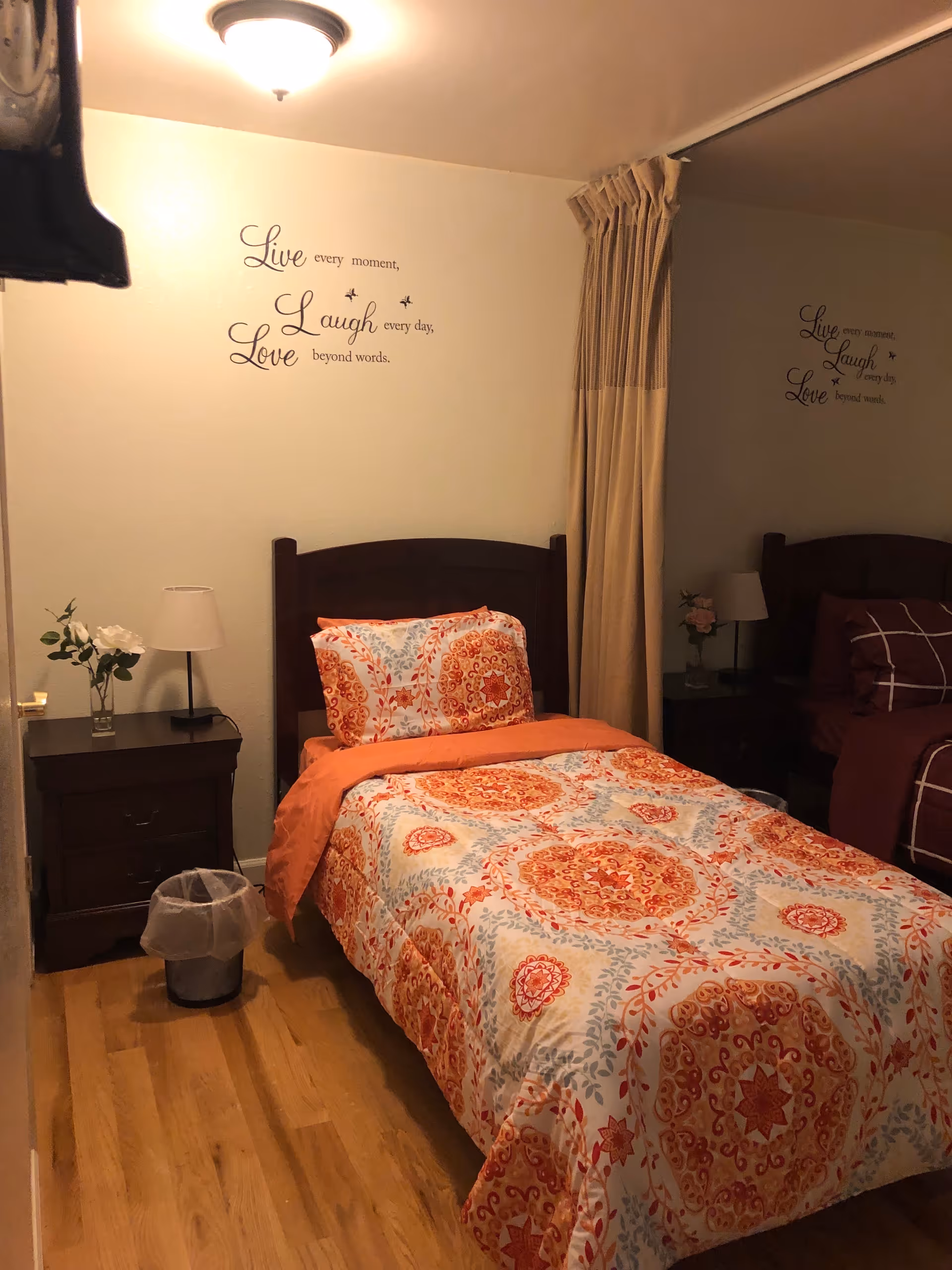 Twin bed with patterned orange and blue bedding in a warmly lit, decorated bedroom.