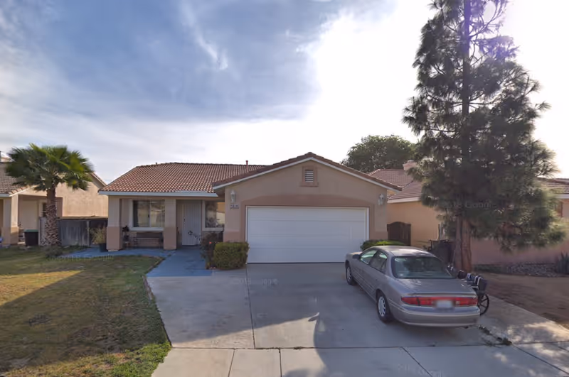 Front view of a single-story house with a driveway, garage, and parked car.