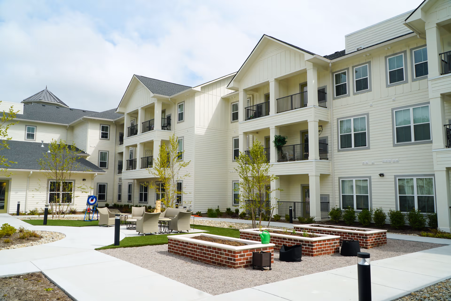 Courtyard with seating, raised brick planters, and balconies in front of a three-story senior living building.