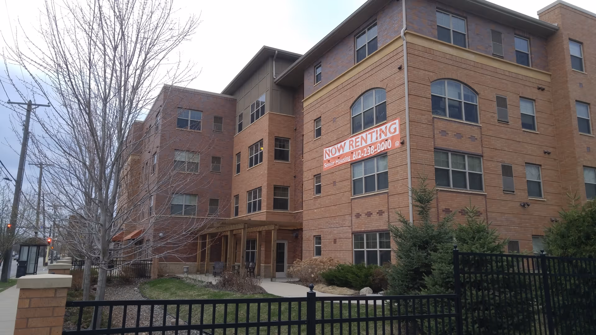 Exterior view of a brick senior living building with a now renting banner.