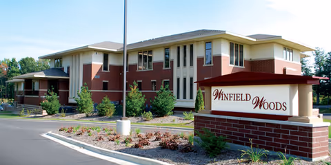 Exterior view of a brick senior living facility with a Winfield Woods sign.