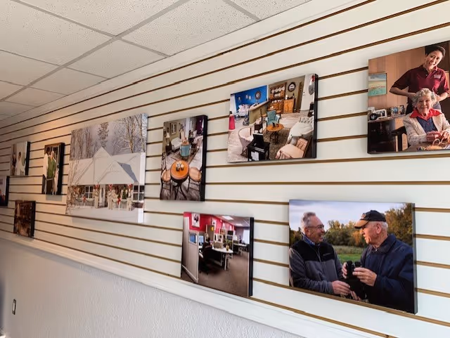 Interior hallway with striped wall displaying framed photos of residents and caregivers.