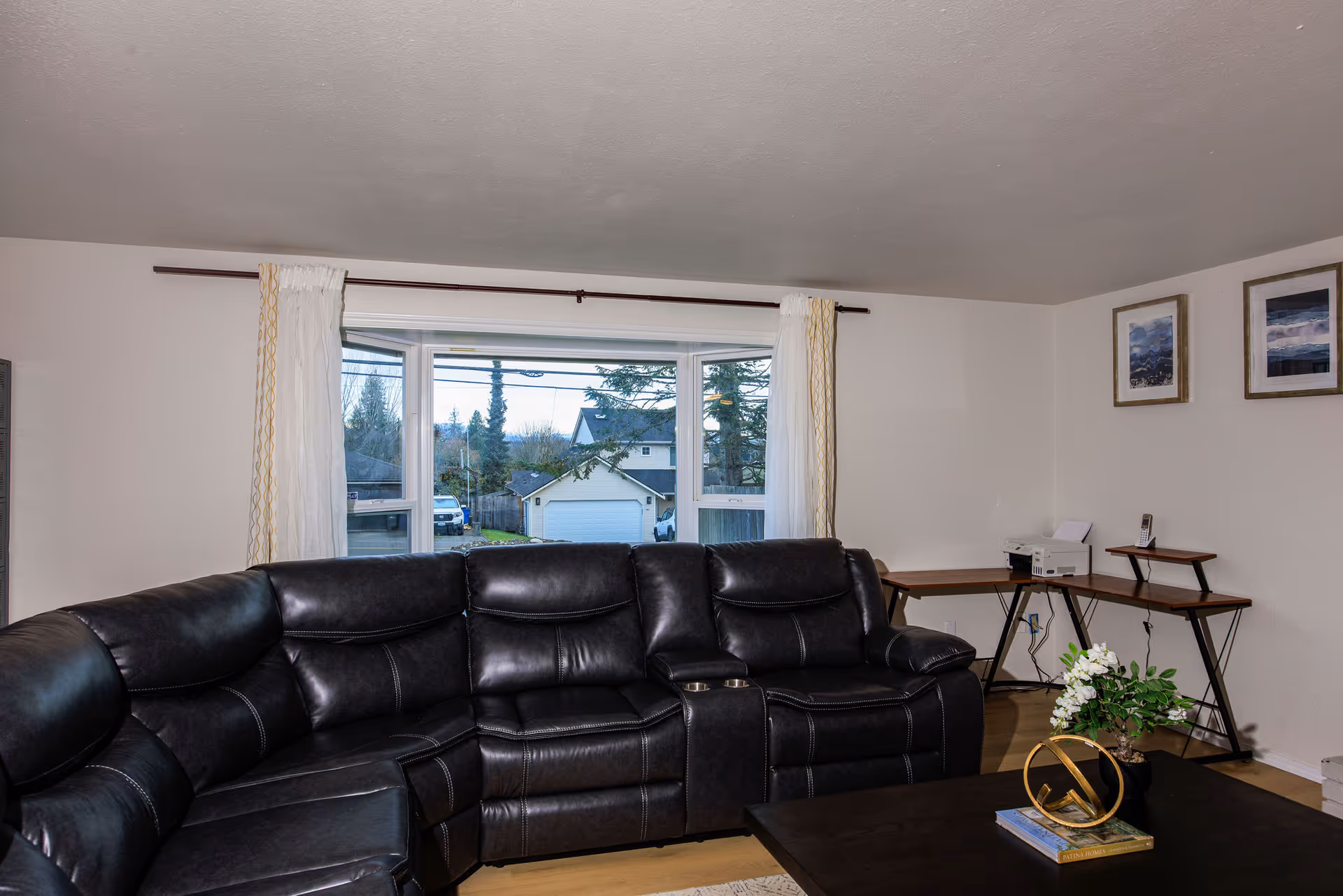 Cozy living room with a black leather sectional, coffee table, and large windowed wall.