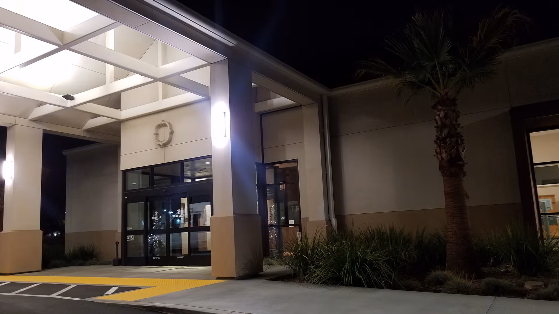 Night exterior of Trellis Chino entrance with glass doors and surrounding landscaping