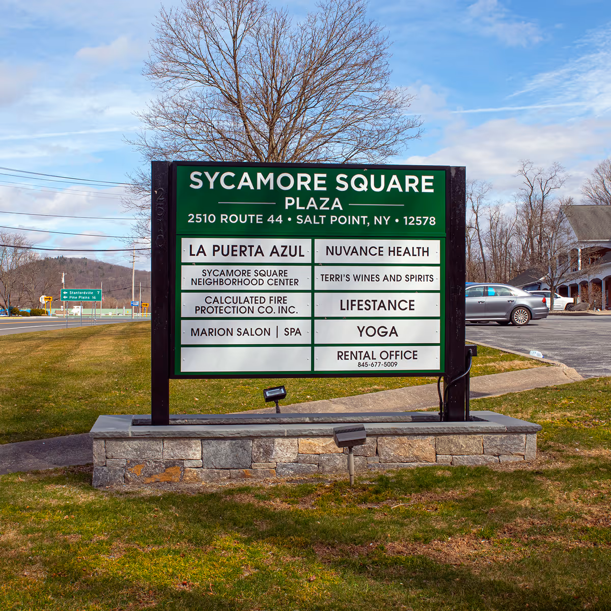 Outdoor sign for Sycamore Square Plaza listing tenants, including Nuvance Health, on a grassy lot.