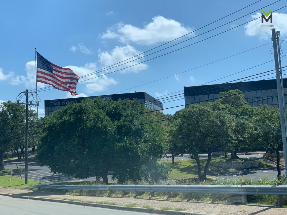 American flag flying over a street lined with trees and office buildings.