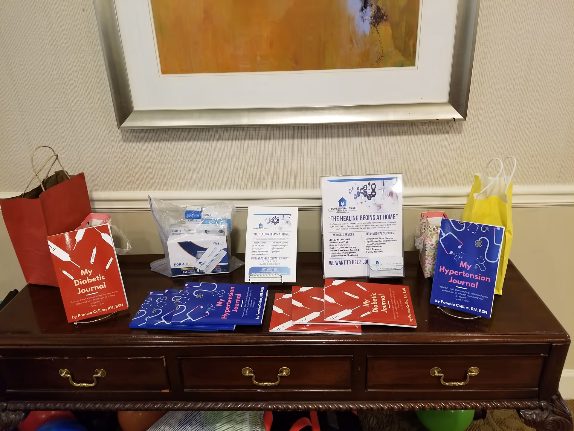 A dark wooden console table displays health journals, pamphlets, and gift bags beneath a framed artwork.