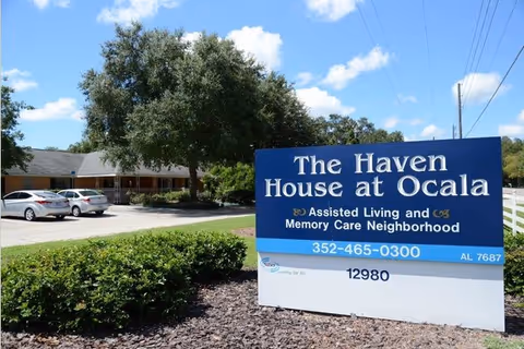 Exterior view of a senior living facility with a blue sign and parked cars.