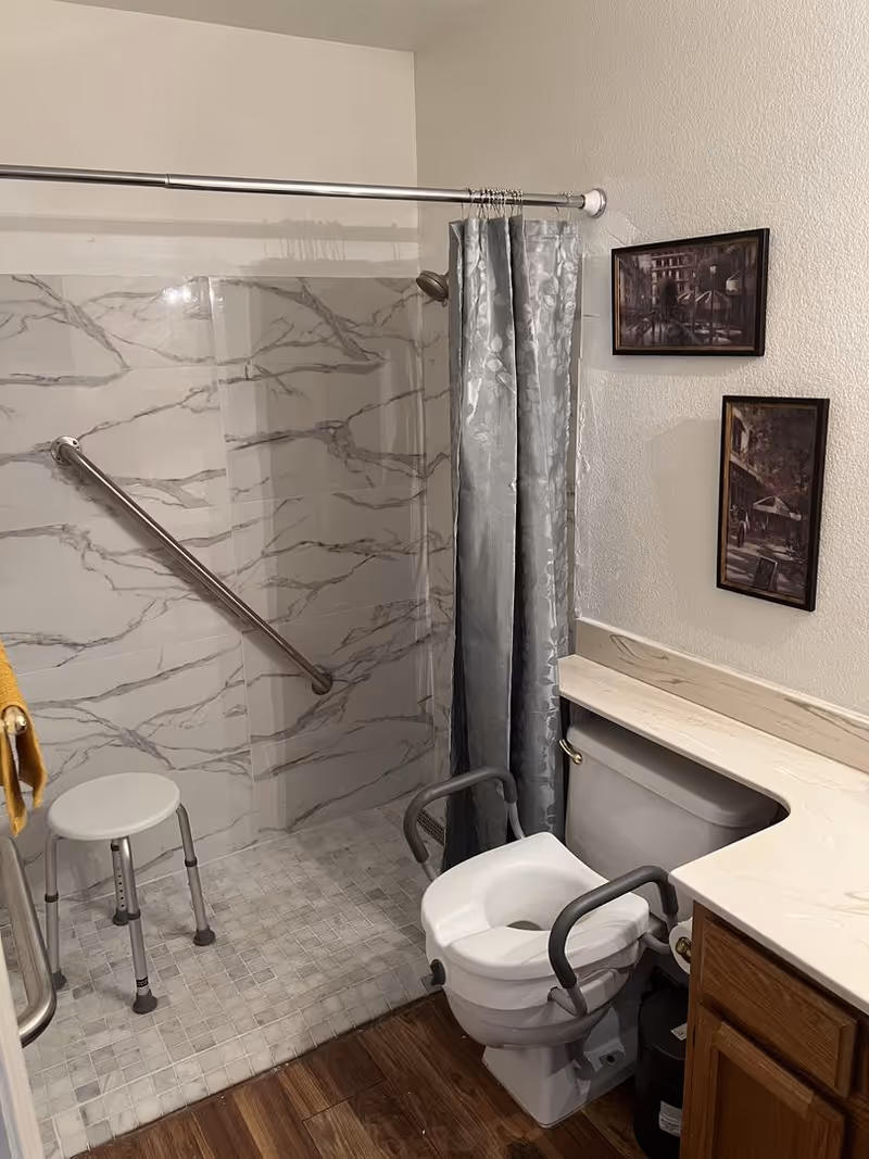 Accessible bathroom with marble-tiled shower, toilet with grab bars, gray curtain, and countertop.